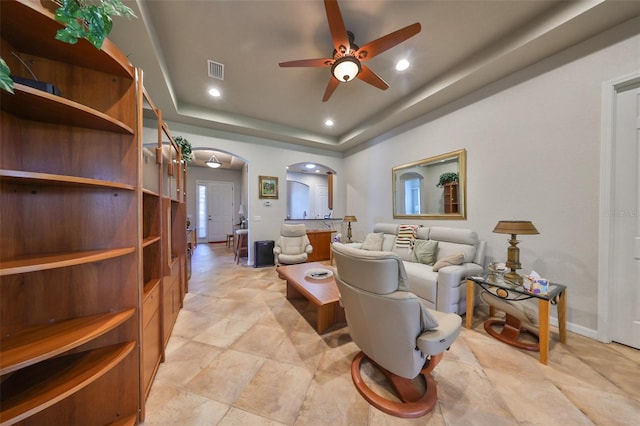 living room featuring a raised ceiling and ceiling fan