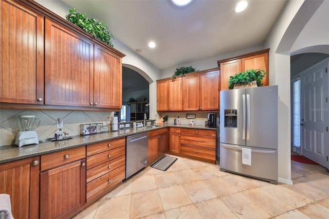 kitchen with appliances with stainless steel finishes, backsplash, sink, light tile patterned floors, and dark stone countertops