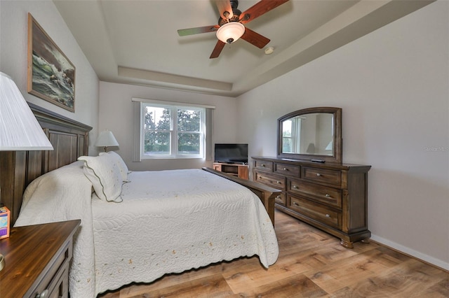 bedroom featuring ceiling fan, light hardwood / wood-style floors, and a raised ceiling