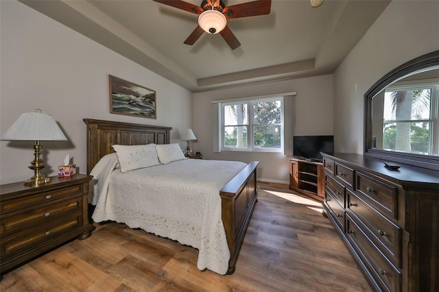 bedroom featuring ceiling fan, dark hardwood / wood-style flooring, multiple windows, and a tray ceiling