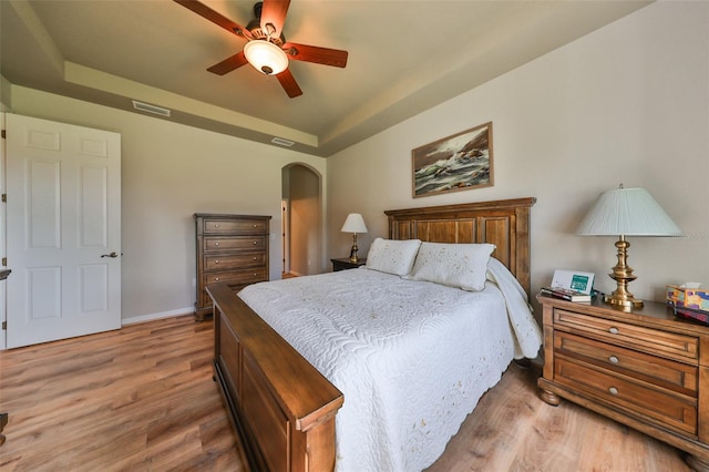 bedroom with light hardwood / wood-style flooring, a raised ceiling, and ceiling fan