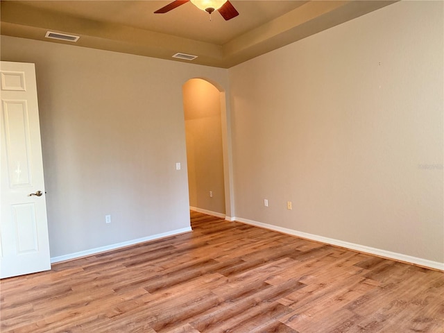 spare room with a tray ceiling, ceiling fan, and light hardwood / wood-style floors