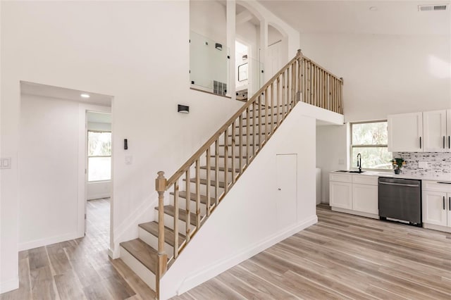 stairs with high vaulted ceiling, a wealth of natural light, sink, and hardwood / wood-style flooring