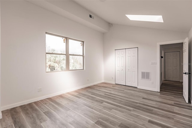 unfurnished bedroom with light hardwood / wood-style floors, vaulted ceiling with skylight, and a closet