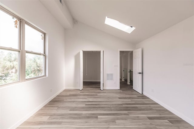 empty room featuring vaulted ceiling with skylight, plenty of natural light, and light hardwood / wood-style flooring