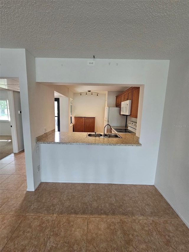 kitchen featuring a textured ceiling, white appliances, light tile patterned floors, sink, and kitchen peninsula