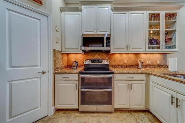 94 The Cove Way, Indian Rocks Beach, FL 33785 - kitchen featuring stainless steel appliances, decorative backsplash, light stone countertops, and glass insert cabinets