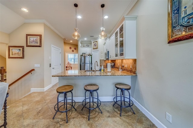 kitchen with white cabinets, ornamental molding, appliances with stainless steel finishes, a kitchen bar, and kitchen peninsula