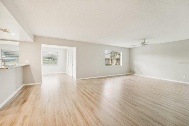 unfurnished living room featuring ceiling fan, light hardwood / wood-style flooring, and a textured ceiling