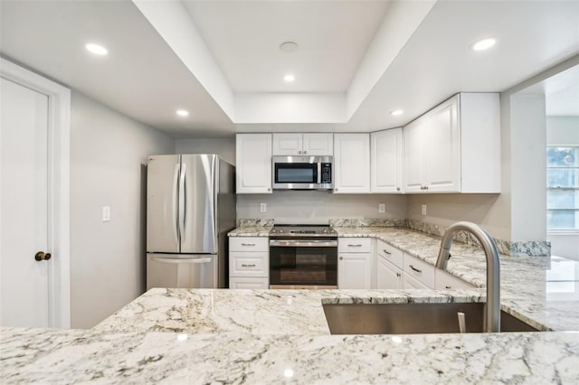 kitchen with white cabinets, a raised ceiling, sink, light stone countertops, and stainless steel appliances