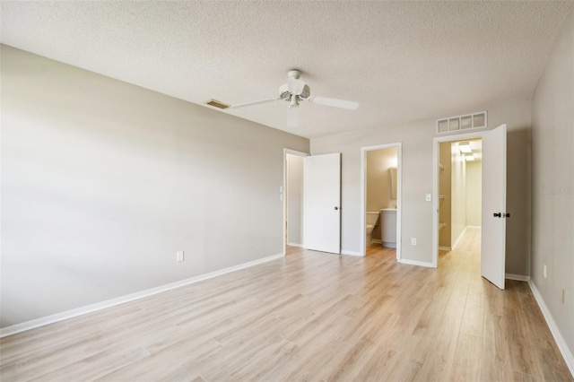 unfurnished bedroom featuring a walk in closet, ensuite bathroom, a textured ceiling, ceiling fan, and light hardwood / wood-style floors