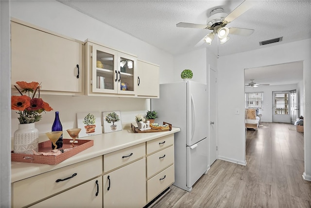 kitchen featuring cream cabinetry, a textured ceiling, light wood-type flooring, and white refrigerator