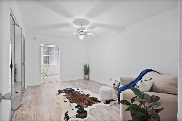 living area with ceiling fan, a textured ceiling, and light wood-type flooring