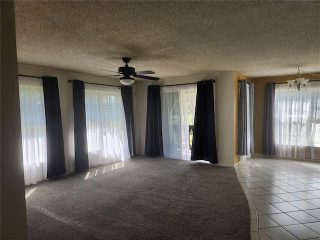 empty room featuring a textured ceiling, light tile patterned floors, and ceiling fan with notable chandelier