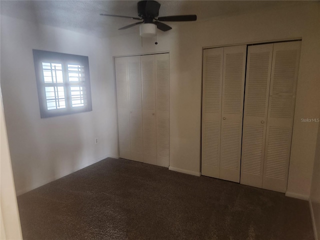 unfurnished bedroom with a textured ceiling, multiple closets, ceiling fan, and dark carpet