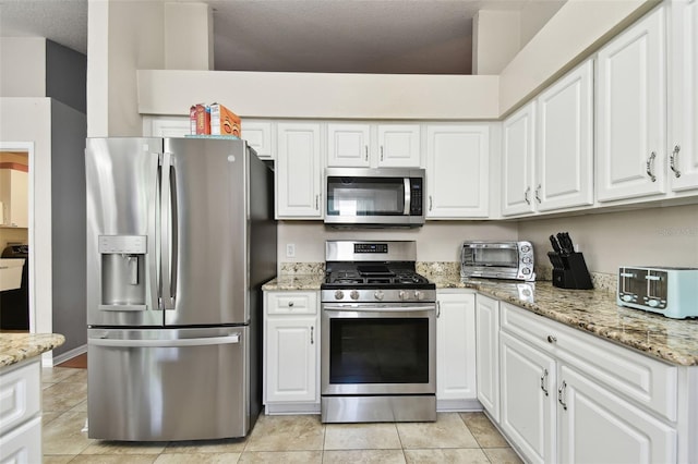 kitchen with white cabinetry, light tile patterned flooring, light stone countertops, and appliances with stainless steel finishes