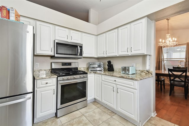 kitchen featuring stainless steel appliances, light hardwood / wood-style flooring, a notable chandelier, pendant lighting, and white cabinets