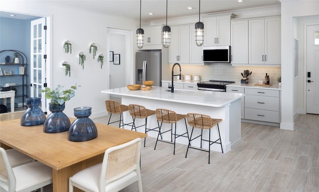 kitchen with stainless steel appliances, a center island with sink, sink, and decorative light fixtures