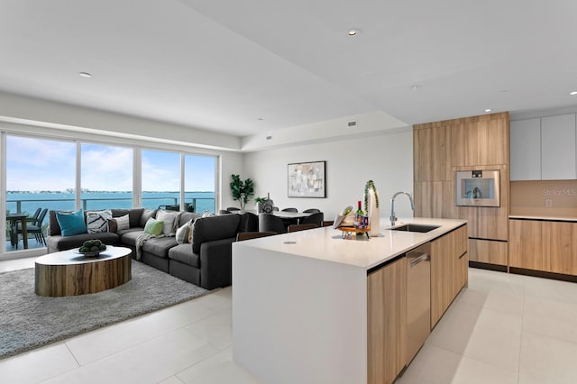 kitchen with sink, light tile patterned floors, a center island with sink, a water view, and white cabinets