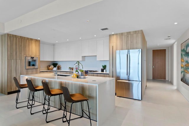 kitchen featuring a kitchen bar, a center island with sink, white cabinets, and stainless steel appliances