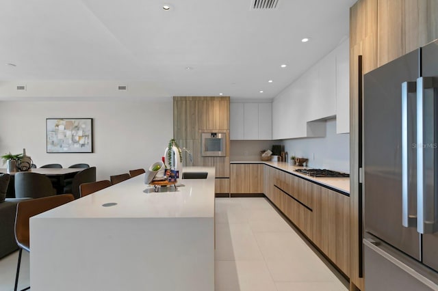 kitchen with white cabinetry, sink, a kitchen bar, a kitchen island with sink, and appliances with stainless steel finishes