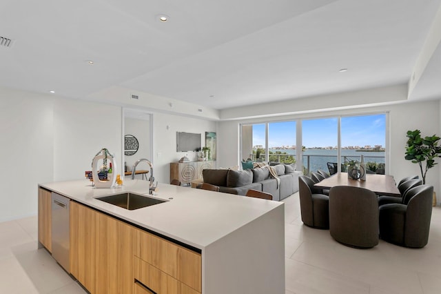 kitchen with sink, dishwasher, a kitchen island with sink, light brown cabinetry, and light tile patterned flooring