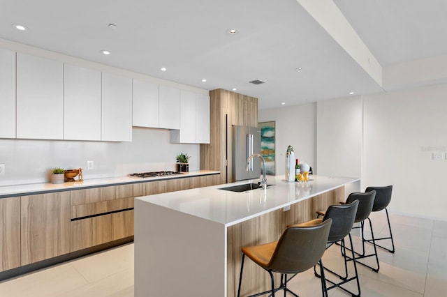 kitchen with a kitchen bar, sink, light tile patterned floors, white cabinets, and an island with sink