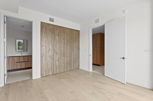 unfurnished bedroom with ensuite bath and light hardwood / wood-style flooring