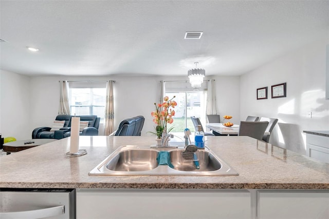 kitchen with pendant lighting, dishwasher, white cabinets, sink, and a notable chandelier