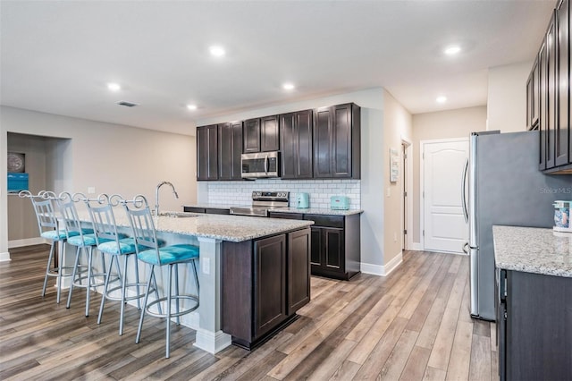 kitchen featuring light stone countertops, sink, light hardwood / wood-style floors, a kitchen island with sink, and appliances with stainless steel finishes