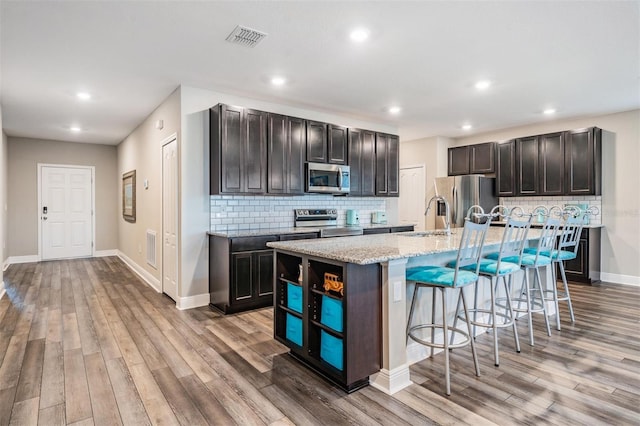 kitchen with a kitchen island with sink, a breakfast bar area, decorative backsplash, appliances with stainless steel finishes, and light wood-type flooring