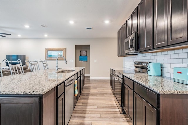 kitchen featuring a center island with sink, sink, decorative backsplash, light wood-type flooring, and appliances with stainless steel finishes