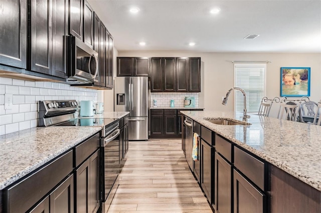 kitchen featuring light stone countertops, sink, light hardwood / wood-style floors, and appliances with stainless steel finishes