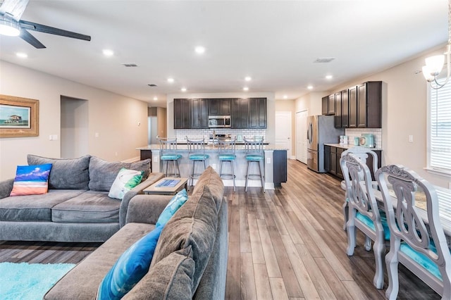 living room with ceiling fan with notable chandelier and light hardwood / wood-style flooring