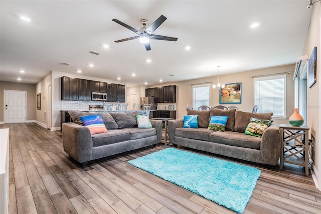 living room featuring ceiling fan with notable chandelier and light wood-type flooring