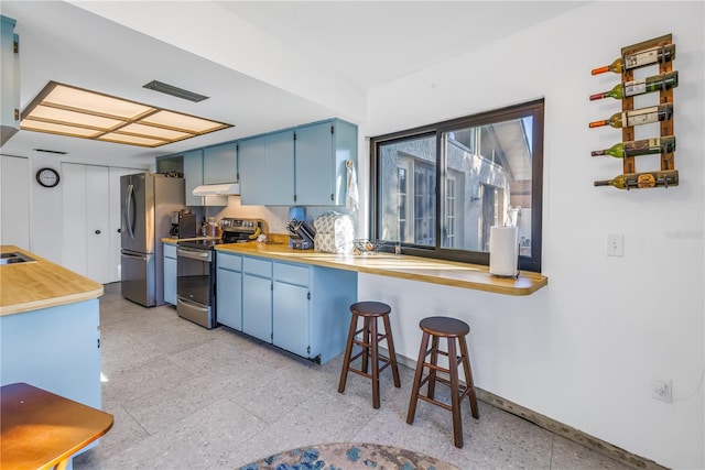 kitchen with kitchen peninsula, appliances with stainless steel finishes, tasteful backsplash, a breakfast bar, and blue cabinets