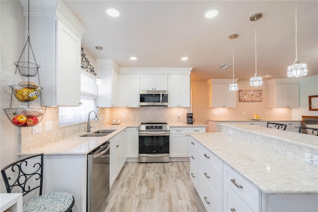 kitchen featuring white cabinets, appliances with stainless steel finishes, decorative light fixtures, and sink