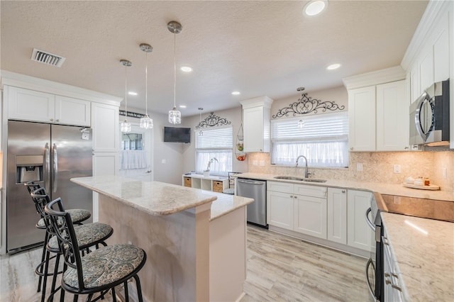 kitchen featuring sink, appliances with stainless steel finishes, decorative light fixtures, white cabinets, and light wood-type flooring