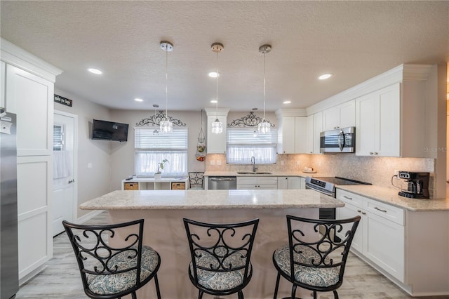 kitchen with pendant lighting, a kitchen island, light stone countertops, and stainless steel appliances