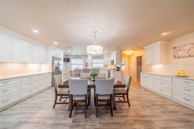 dining space with an inviting chandelier, a textured ceiling, and light wood-type flooring