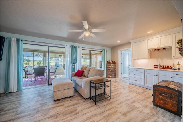 living room with ceiling fan, light hardwood / wood-style floors, and a textured ceiling