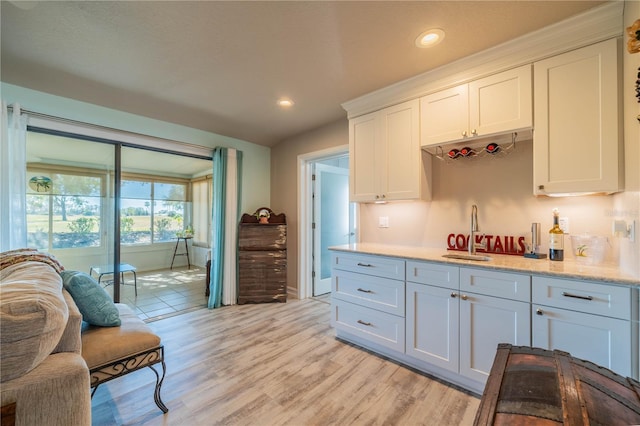 kitchen with light stone counters, light hardwood / wood-style flooring, white cabinetry, and sink