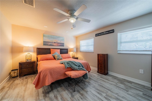 bedroom with ceiling fan, light wood-type flooring, and a textured ceiling