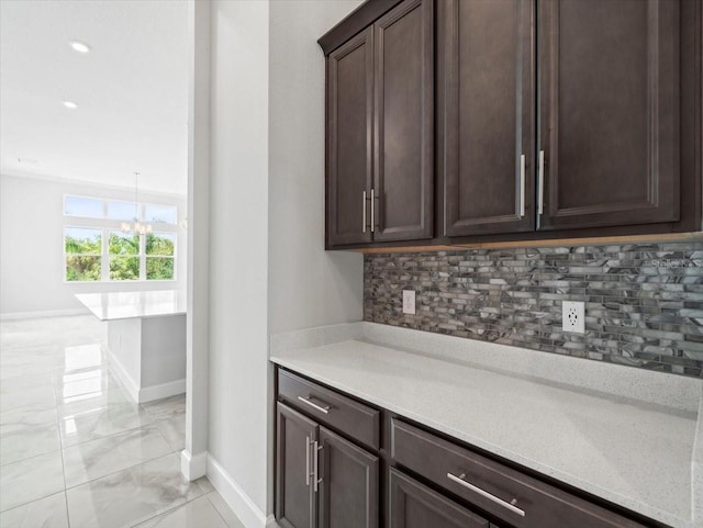 bar with tasteful backsplash, light stone countertops, dark brown cabinets, and a notable chandelier