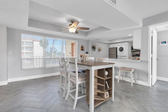 kitchen with kitchen peninsula, ceiling fan, stacked washer / drying machine, white cabinetry, and stainless steel appliances