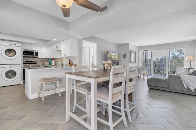 dining area featuring sink, light parquet floors, stacked washer / dryer, and ceiling fan