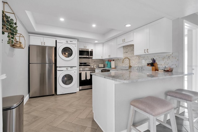 kitchen featuring tasteful backsplash, stacked washer and dryer, white cabinets, and stainless steel appliances