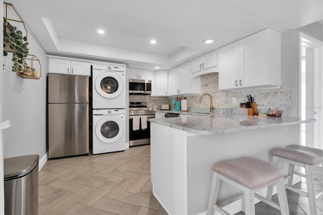 9000 Commodore Dr Unit 401, Seminole, FL 33776 - kitchen with appliances with stainless steel finishes, stacked washer / drying machine, a peninsula, white cabinets, and a kitchen breakfast bar