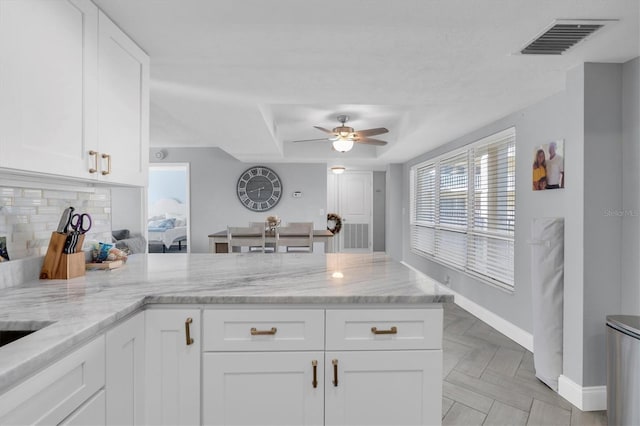 kitchen with white cabinets, ceiling fan, decorative backsplash, light stone counters, and kitchen peninsula