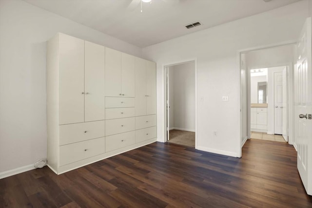 unfurnished bedroom with ceiling fan, ensuite bathroom, and dark wood-type flooring